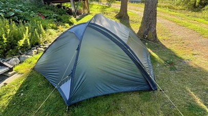  Grey tent pitched on grass in sunlight, surrounded by trees and nature.