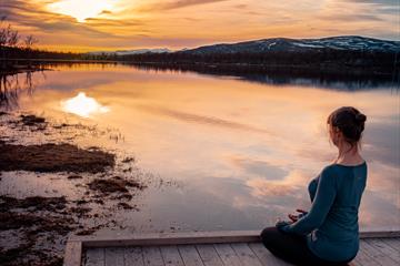 A woman practising mindfulness next to a mountain lake