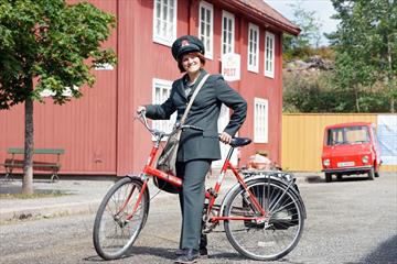 Postbud i historisk uniform og sykkel foran Postgården på Maihaugen.