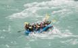 Group in a rafting boat paddling through strong rapids.