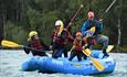 Family paddling a rafting boat on a river, with a guide at the back.