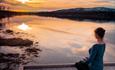 A woman practising mindfulness next to a mountain lake