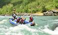 Rafting boat in whitewater rapids surrounded by mountains and forest.
