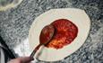Tomatensoße wird auf Pizzateig verteilt.