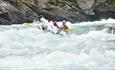 Rafting boat in powerful rapids between rocky cliffs.