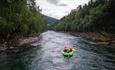 Raftingflåte midt i strømmen på Sjoa-elva, med skogkledde dalsider på begge sider.
