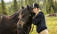 A young woman smiles towards the camera with her horse