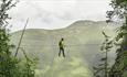Person crossing a high-wire bridge in the mountains.