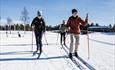 Two people cross-country skiing on a groomed track