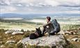Person sitter på stein og ser utover fjellandskap