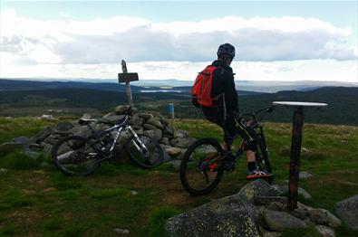 Mountain biker at the top of the mountian Snørvillen at Sjusjøen with a view towards mountains mountains in the distance.