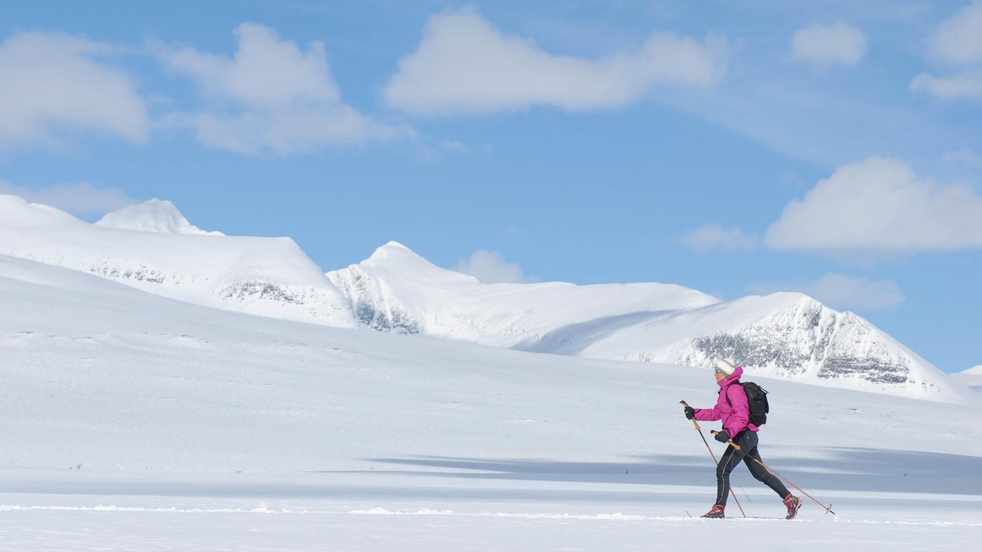 Kvinne på ski i forgrunnen fremfor de majestetiske fjellene i Rondane.