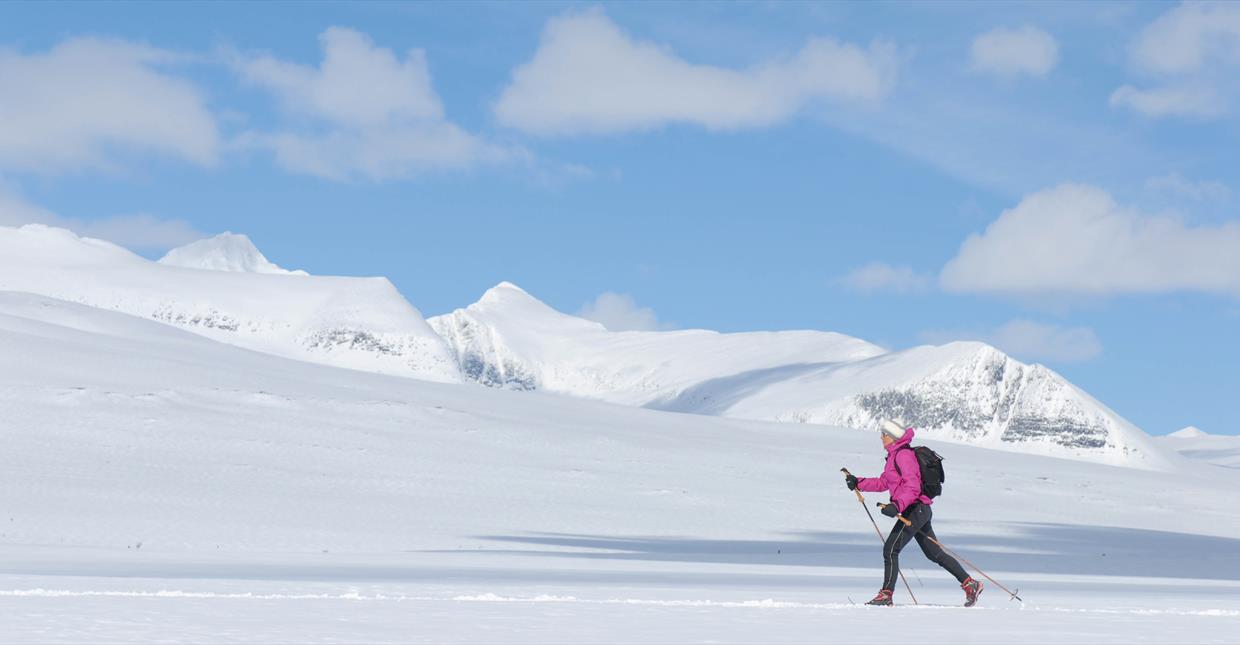 Kvinne på ski i forgrunnen fremfor de majestetiske fjellene i Rondane.