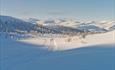 Solskinn, snø og skiløyper. 2 personer på langrennski. Fjell i bakgrunnen. Spidsbergseter Resort Rondane.