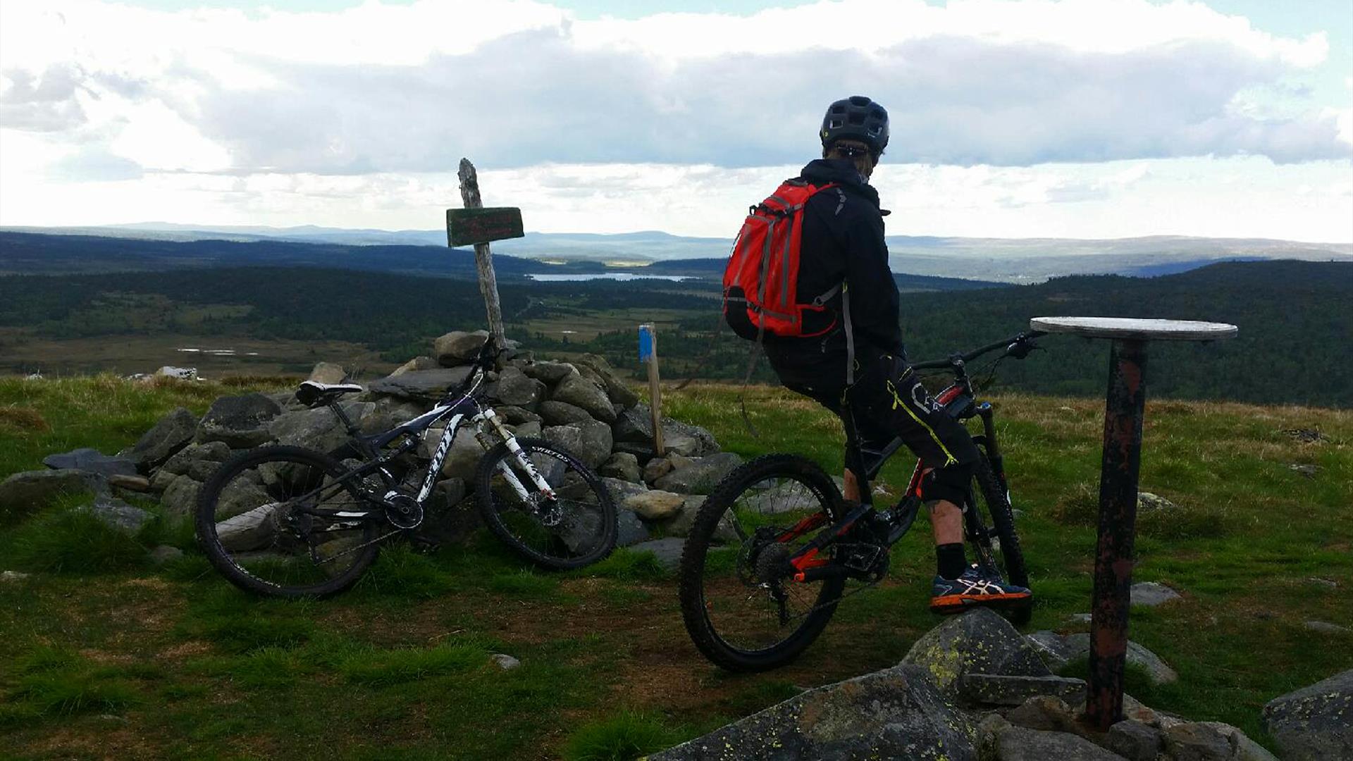 Mountain biker at the top of the mountian Snørvillen at Sjusjøen with a view towards mountains mountains in the distance.