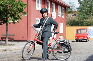 Postbud i historisk uniform og sykkel foran Postgården på Maihaugen.