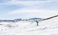 Kid in green dress skiing down the alpine slope. Easter snow and sunshine. Spidsbergseter resort Rondane