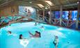 Blå pool med folk som svømmer. Bro over poolen. Spidsbergseter Resort Rondane.