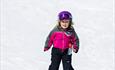 Jente med rosa jakke står på alpint i skisenteret. Sol og påskesnø- Spidsbergseter Resort Rondane