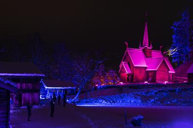 Garmo stavkirke lyssatt i rødt lys en vinterkveld.