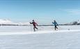 To skiløpere i fint driv bortover i vinterlandskap.