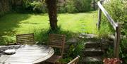 The back garden at Sunflowers Barn showing a table and chairs and steps leading to the lawn