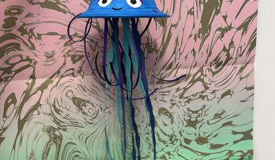 A jellyfish made from an upside down paper bowl and paper tentacles in front of a swirly background