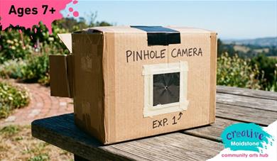 Pinhole camera made of cardboard on a wooden table with scenery in the background