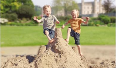 Two boys jumping on a sandcastle.