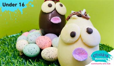 Two chocolate Easter eggs with googly eyes sitting on a nest of chocolate mini eggs on grass with a green background