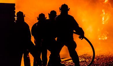 Firefighters silhouetted against a fire background