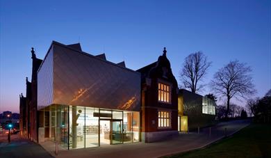 Photograph of the outside of Maidstone Museum taken at dusk with dark sky and lights inside