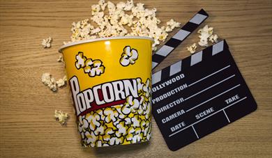 Bucket of popcorn on its side with popcorn spilling out next to a clapper board