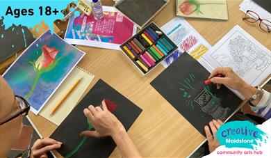 An art class with hands working on chalk drawings and art materials on the table