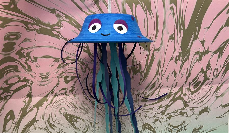 A jellyfish made from an upside down paper bowl and paper tentacles in front of a swirly background