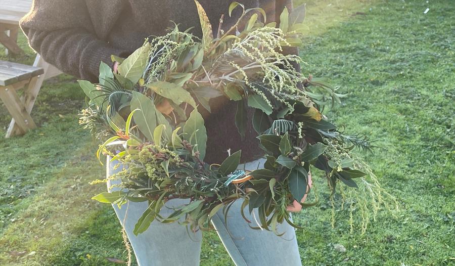 A workshop participant holding a wreath made from willow and seasonal foliage.