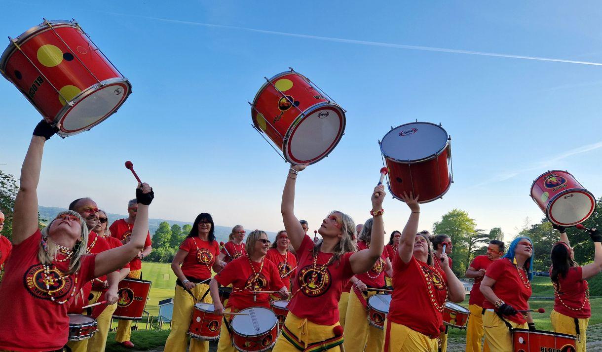 Group of people wearing bright clothes holding samba drums in the air