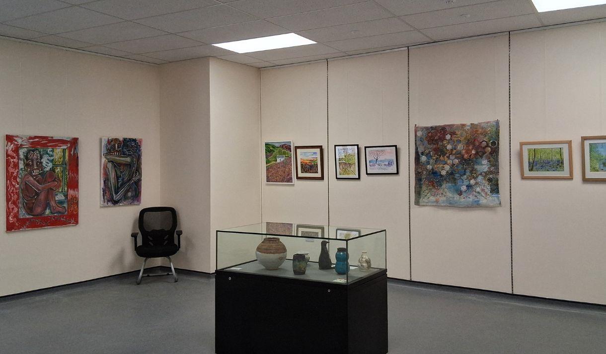View of an exhibition gallery with artworks on the wall and a display cabinet in front