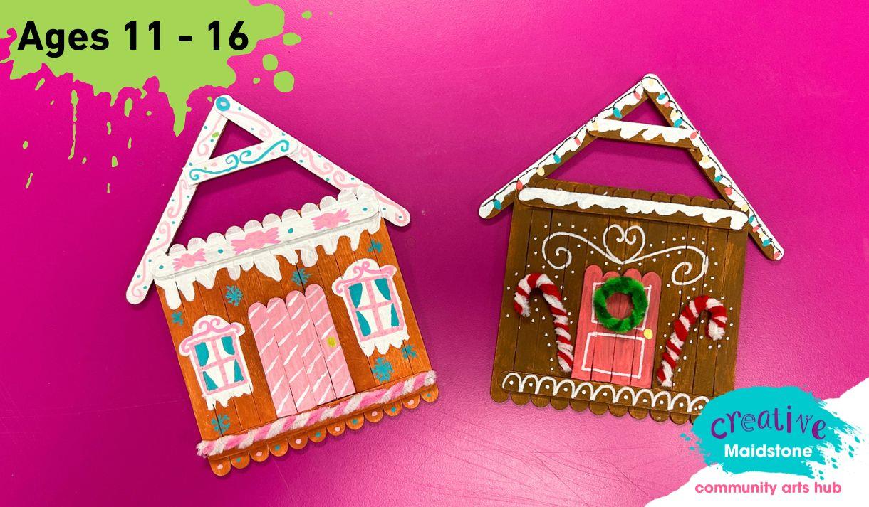 Two gingerbread house tree decorations made out of lollipop sticks on a pink background