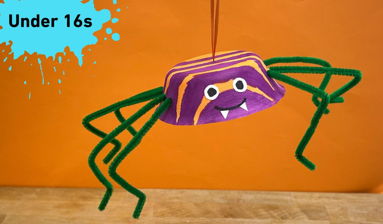 Paint splat in the top left corner with under 16s in black text. Main image an orange and Black spider made from a paper bowl