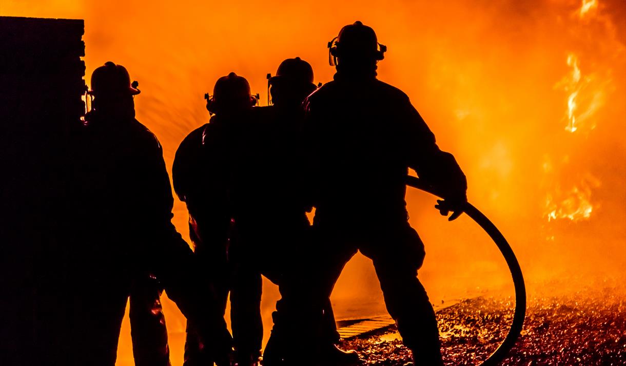 Firefighters silhouetted against a fire background