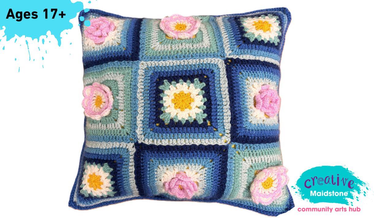 A crochet cushion in blues and greys with crochet flowers on