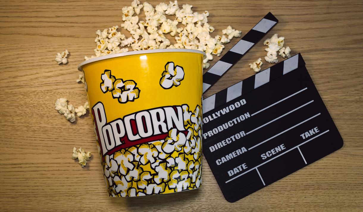Bucket of popcorn on its side with popcorn spilling out next to a clapper board