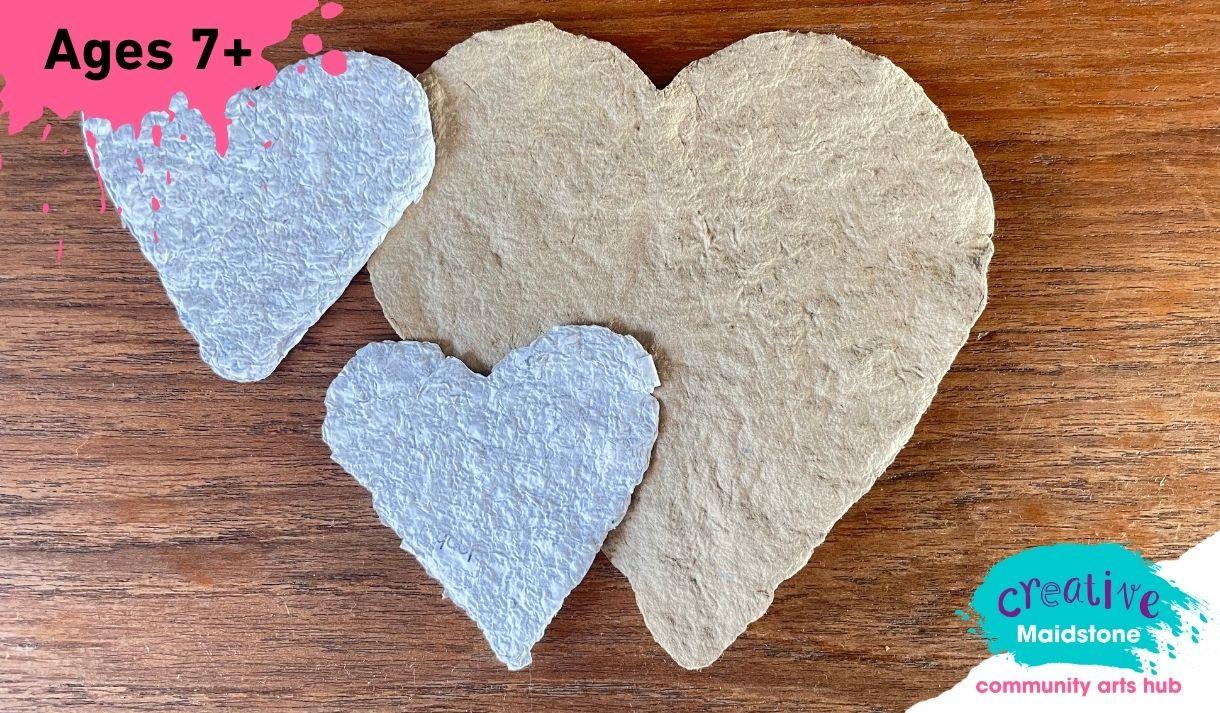 Three heart-shaped pieces of handmade paper on a wooden background