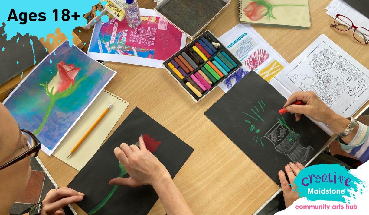 An art class with hands working on chalk drawings and art materials on the table