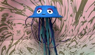 A jellyfish made from an upside down paper bowl and paper tentacles in front of a swirly background