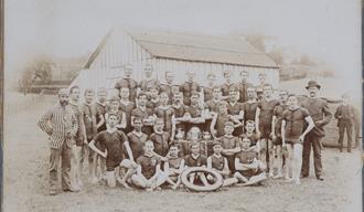 Sepia toned group photograph of Maidstone Swimming Club members, all males in swimming costumes, standing, kneeling or sitting in five rows, a life-fl