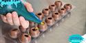 Hand holding a piping bag squeezing liquid caramel into a preformed chocolate ball shell