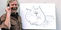 Tony Hart standing in front of a drawing of a cartoon cat, holding a large pen
