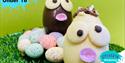 Two chocolate Easter eggs with googly eyes sitting on a nest of chocolate mini eggs on grass with a green background